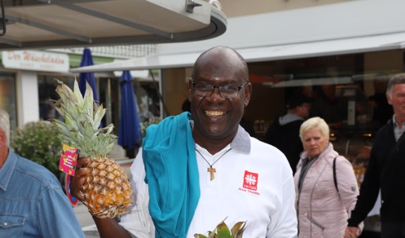 Pater Primus am Marktstand mit einer Ananas in der Hand, © Hartmut Wolf