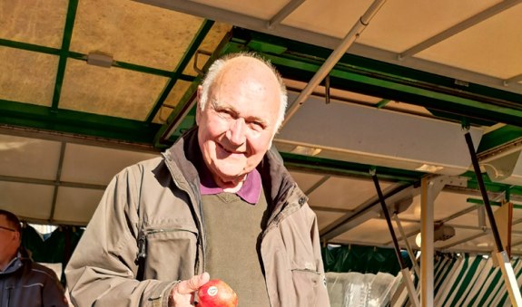 Hans Günther Kaufmann steht am Marktstand mit Apfel in der Hand, © Kulturamt der Stadt Miesbach